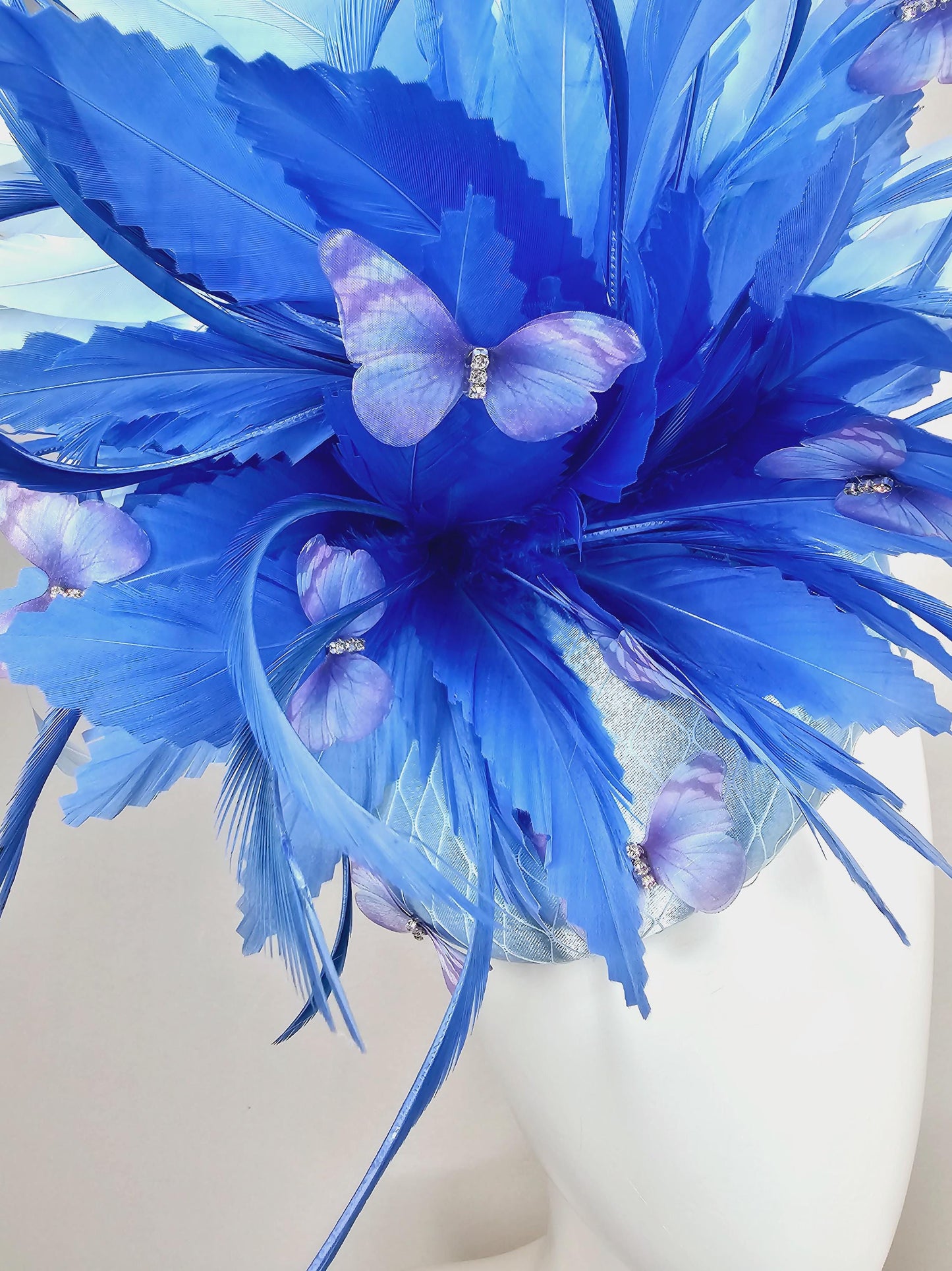 kentucky derby hat fascinator light blue satin with netting, fluffy zigzag royal blue and light blue branching feathers, purple butterflies