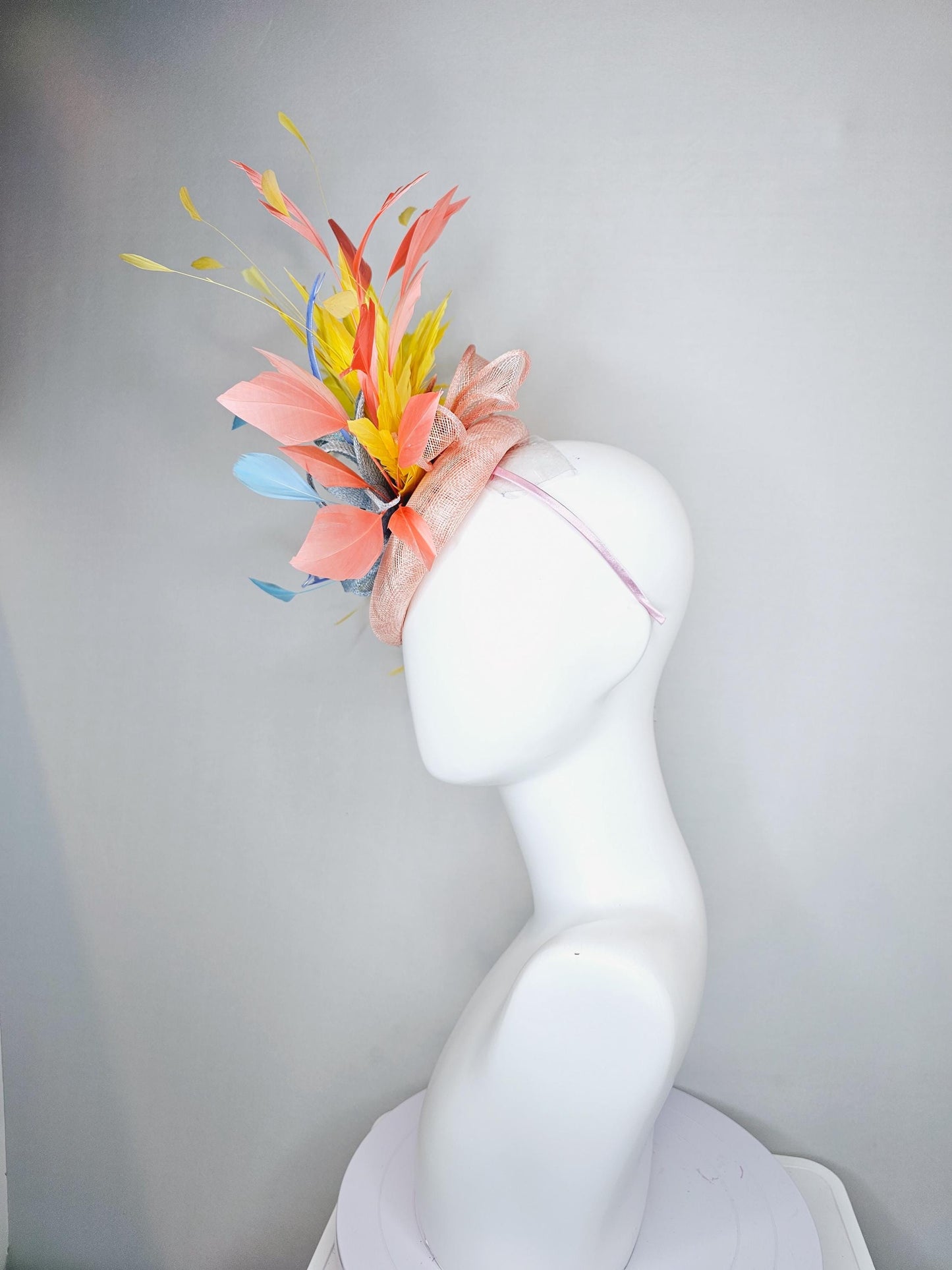 kentucky derby hat fascinator light pink sinamay with light blue sinamay bow and blue feathers, coral orange and yellow branching feathers