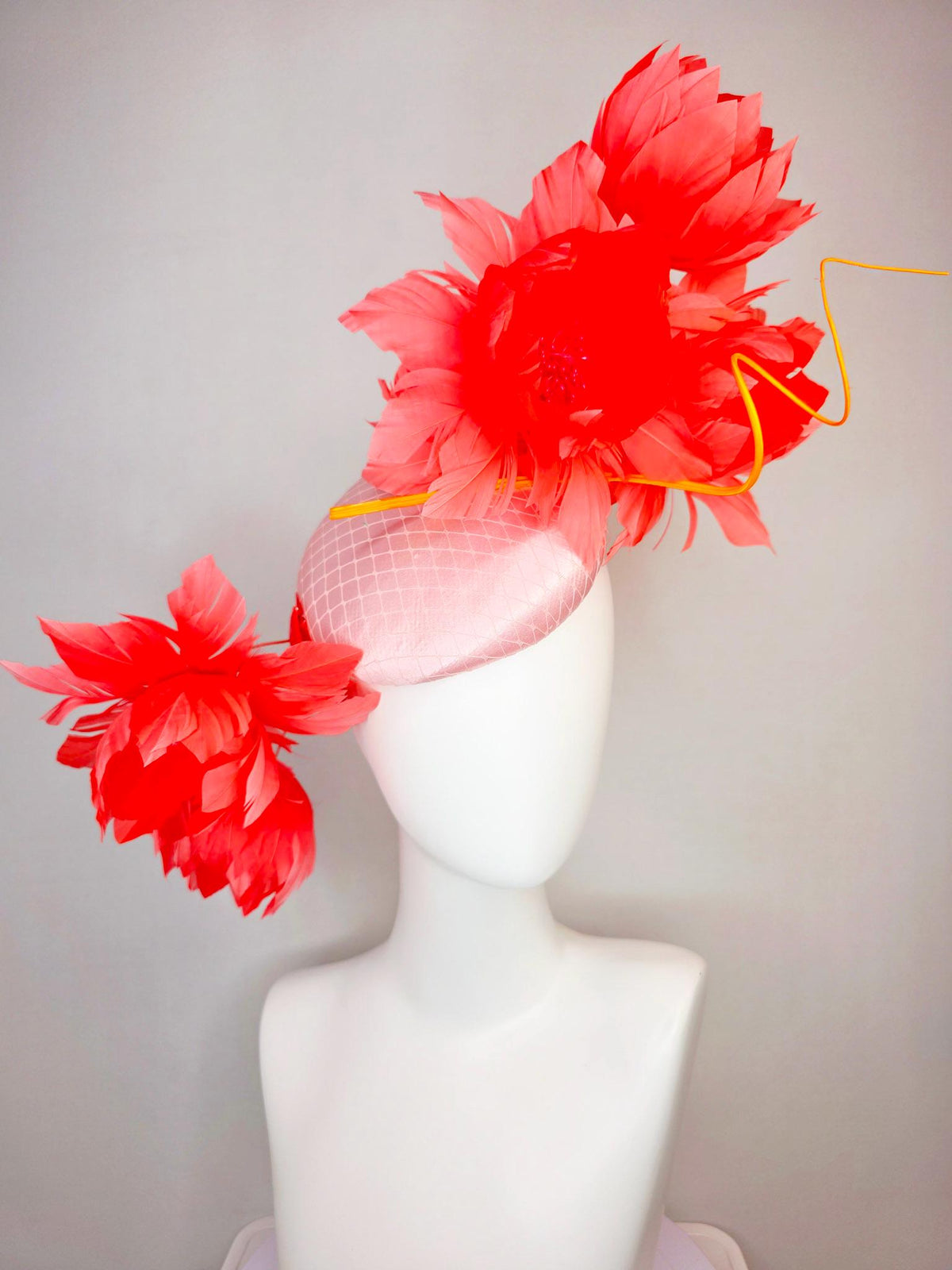 kentucky derby hat fascinator light pink satin with netting and large fluffy coral red feather flowers and light peach orange feathers