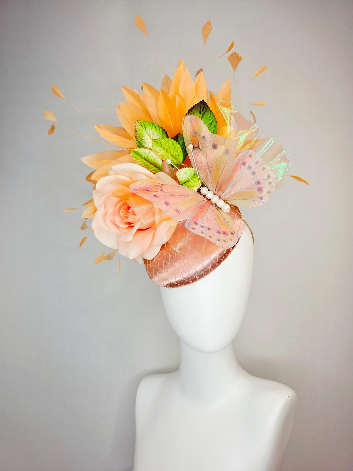 kentucky derby hat fascinator champagne pink satin with netting light pink satin rose green leaves burnt orange feathers and large butterfly