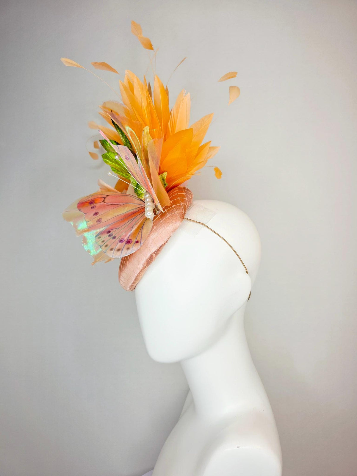 kentucky derby hat fascinator champagne pink satin with netting light pink satin rose green leaves burnt orange feathers and large butterfly